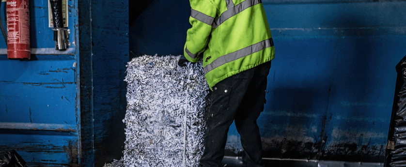 A man wearing a yellow jacket stands next to a large pile of paper designated for confidential shredding.